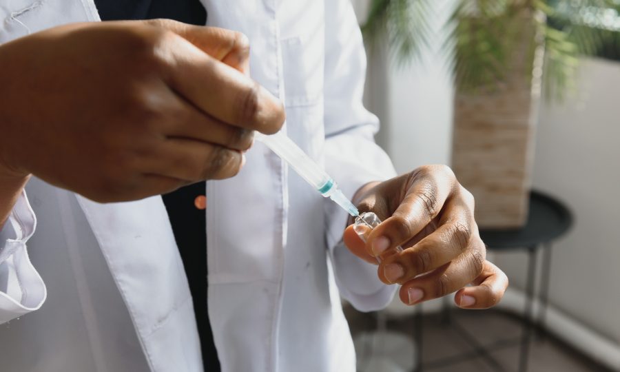 healthcare and medical concept - african doctor holding syringe with injection.